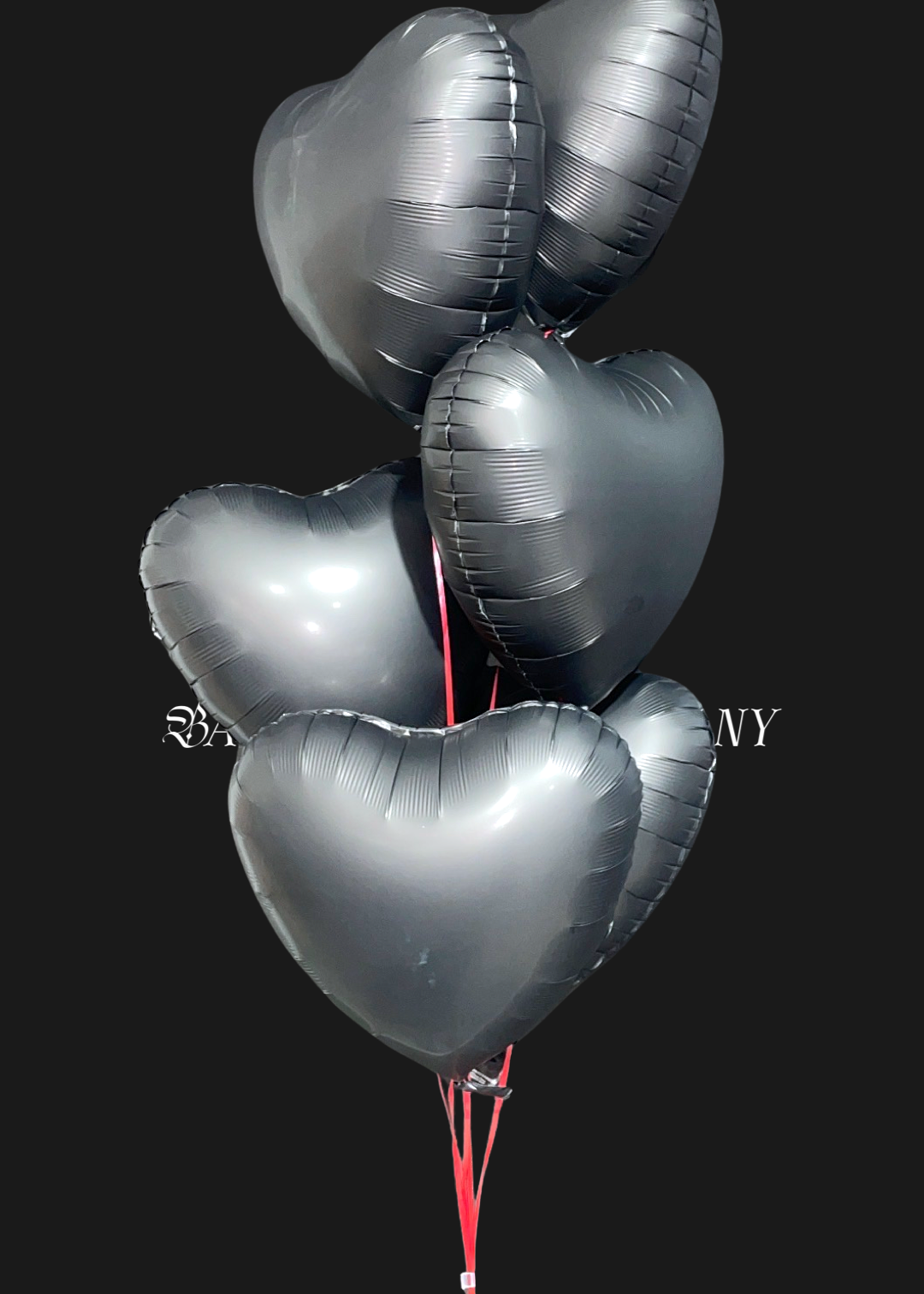 Seven matte black heart-shaped balloons tied together with a string on a black background