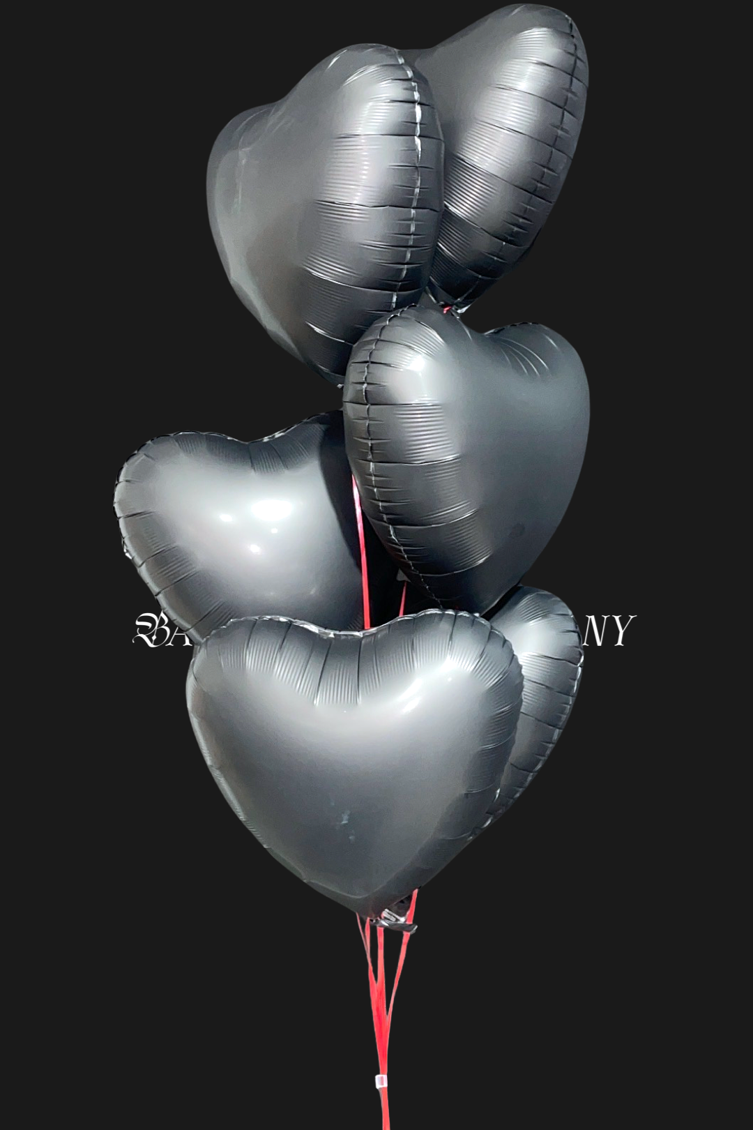Seven matte black heart-shaped balloons tied together with a string on a black background