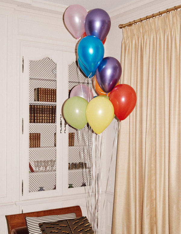 Colorful balloons tied to a chair against a white wall with a window.