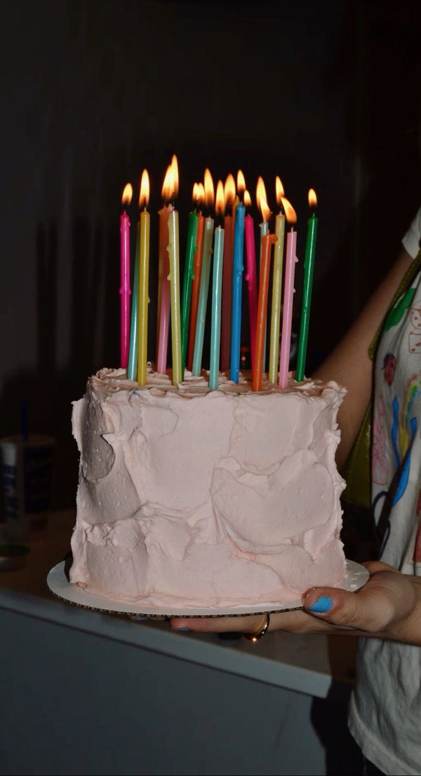 Person holding a birthday cake with lit candles in front of a dark background